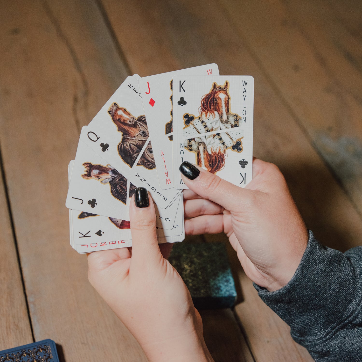 Hands holding playing cards with horse designs on a wooden surface