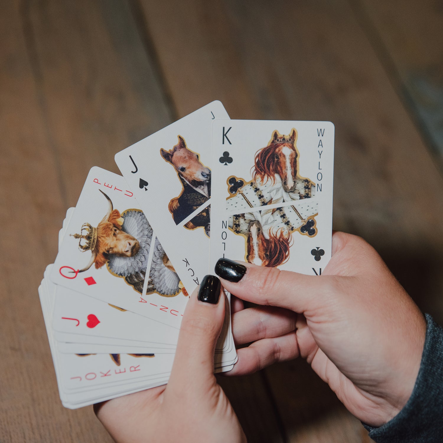 Hands holding playing cards with horse designs on a wooden surface